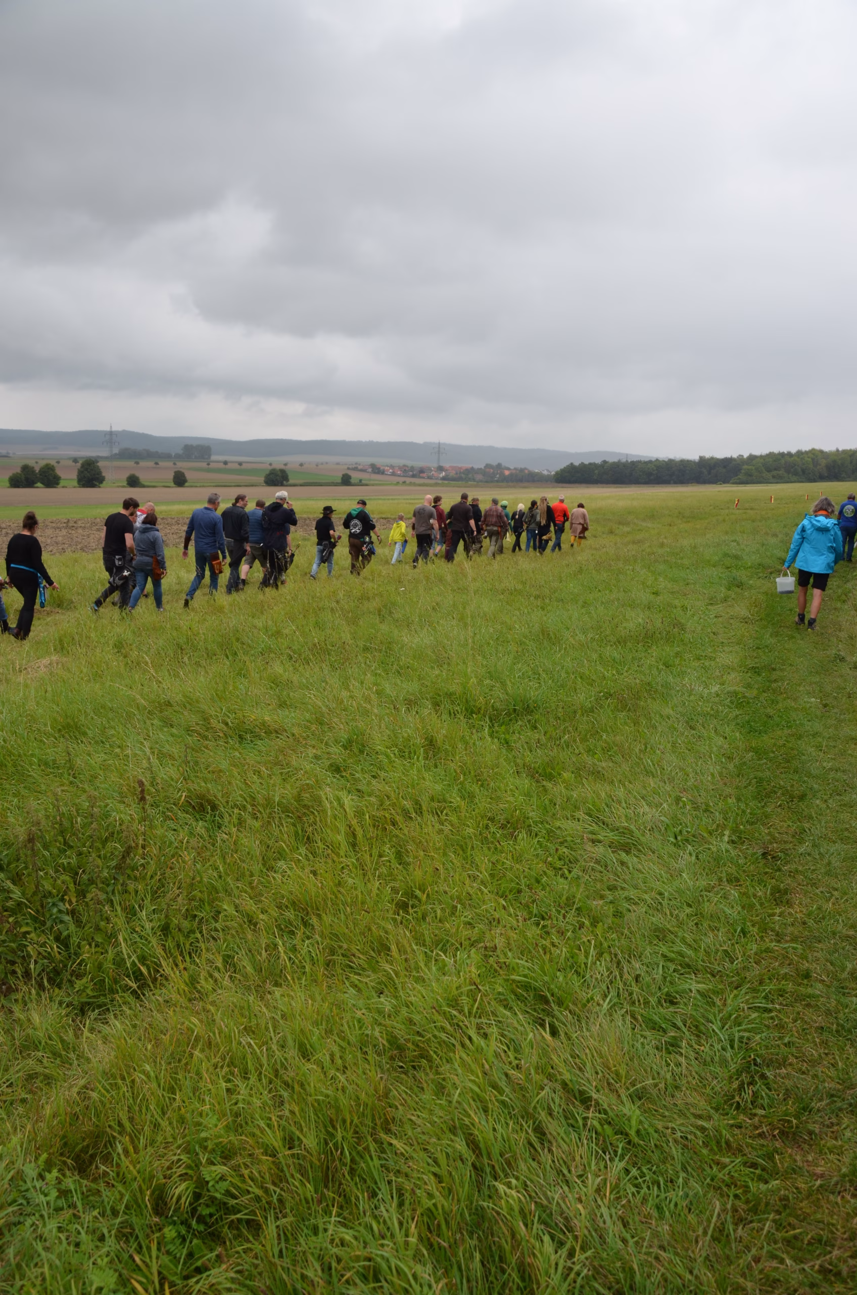Gruppe von Bogenschützen beim Siebenberge Clout Bogenwettbewerb 2021, die ein weites grünes Feld unter bewölktem Himmel durchquert. Veranstaltet von Pfeilflugkunst.