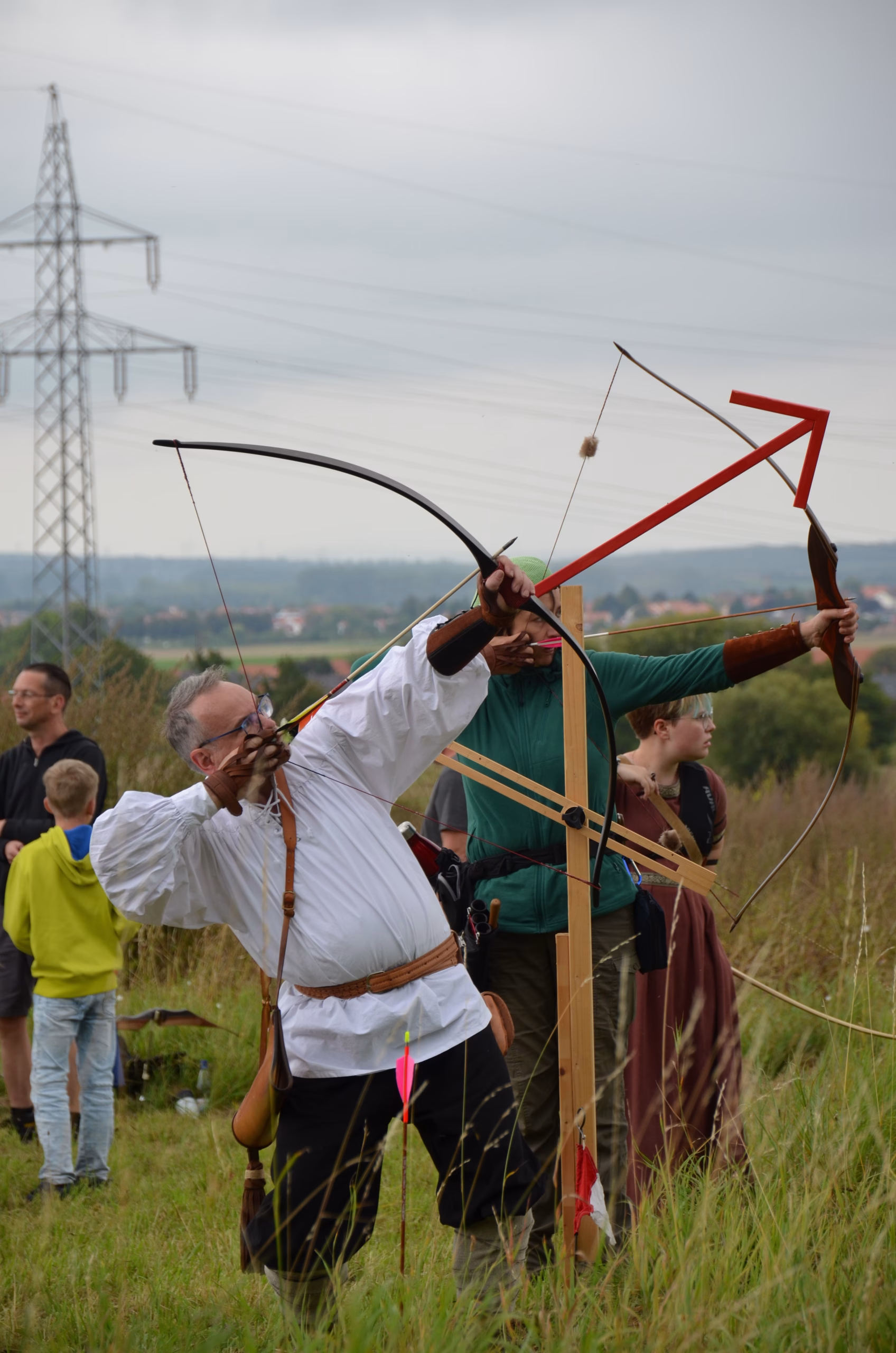 Zwei Bogenschützen in traditioneller Kleidung beim Clout-Bogenschießen während des Siebenberge Clout Bogenwettbewerbs 2021 von Pfeilflugkunst.