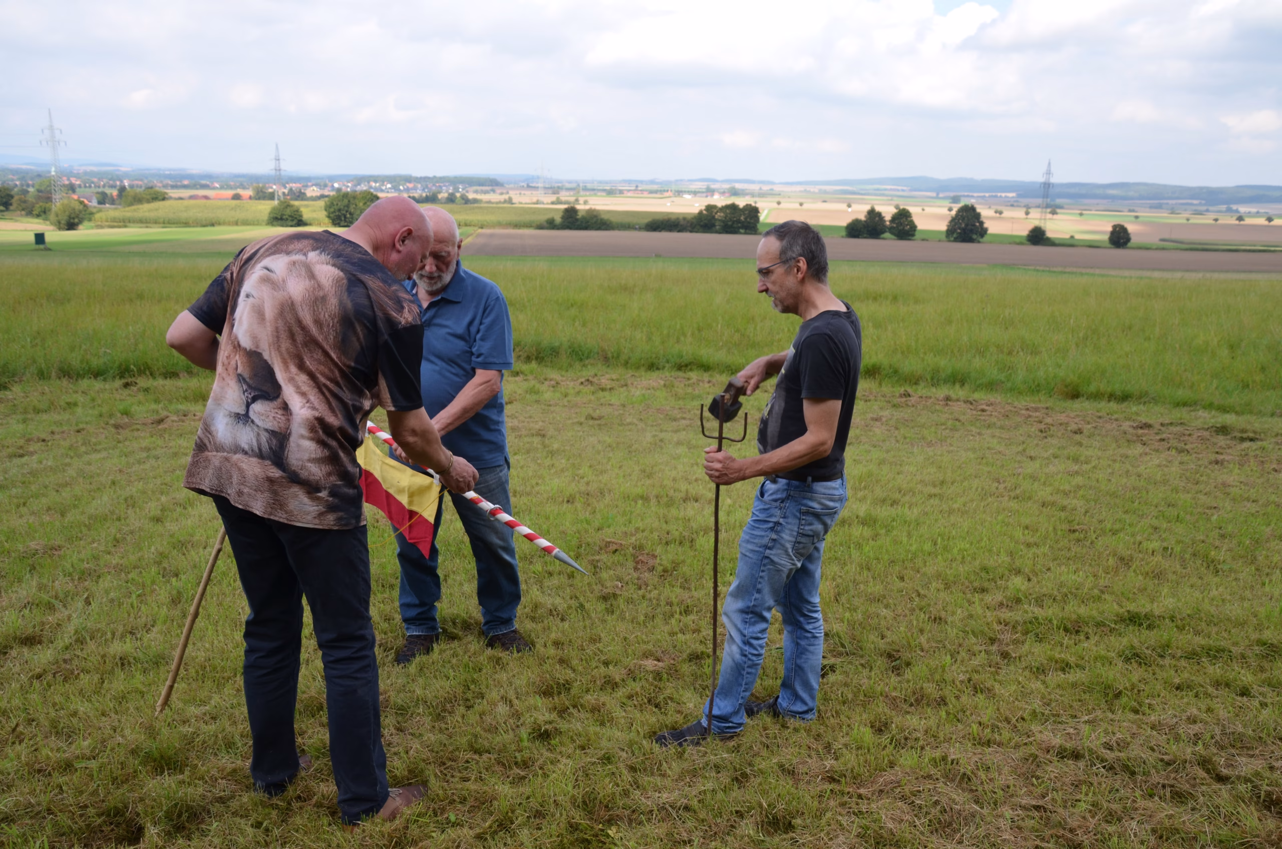 Drei Männer positionieren die Clout-Flagge für den Bogenschießwettbewerb von Pfeilflugkunst in Siebenberge.