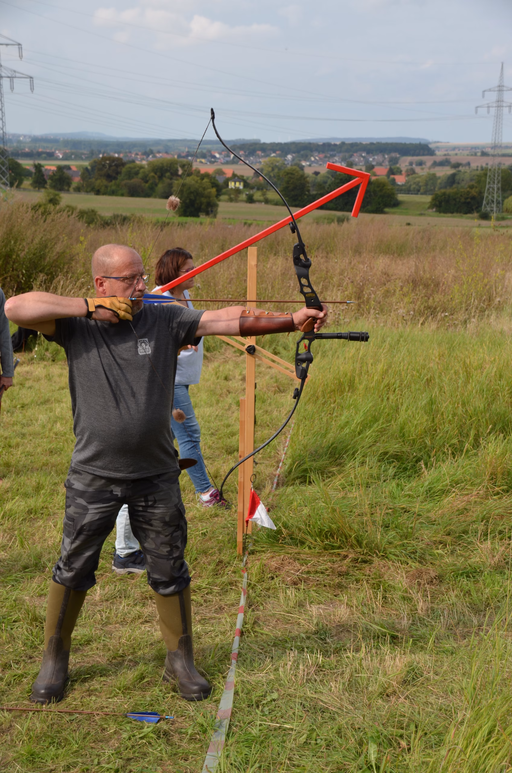 Bogenschütze in Gummistiefeln spannt Bogen beim Clout-Bogenschießen des Pfeilflugkunst-Wettbewerbs in Siebenberge.
