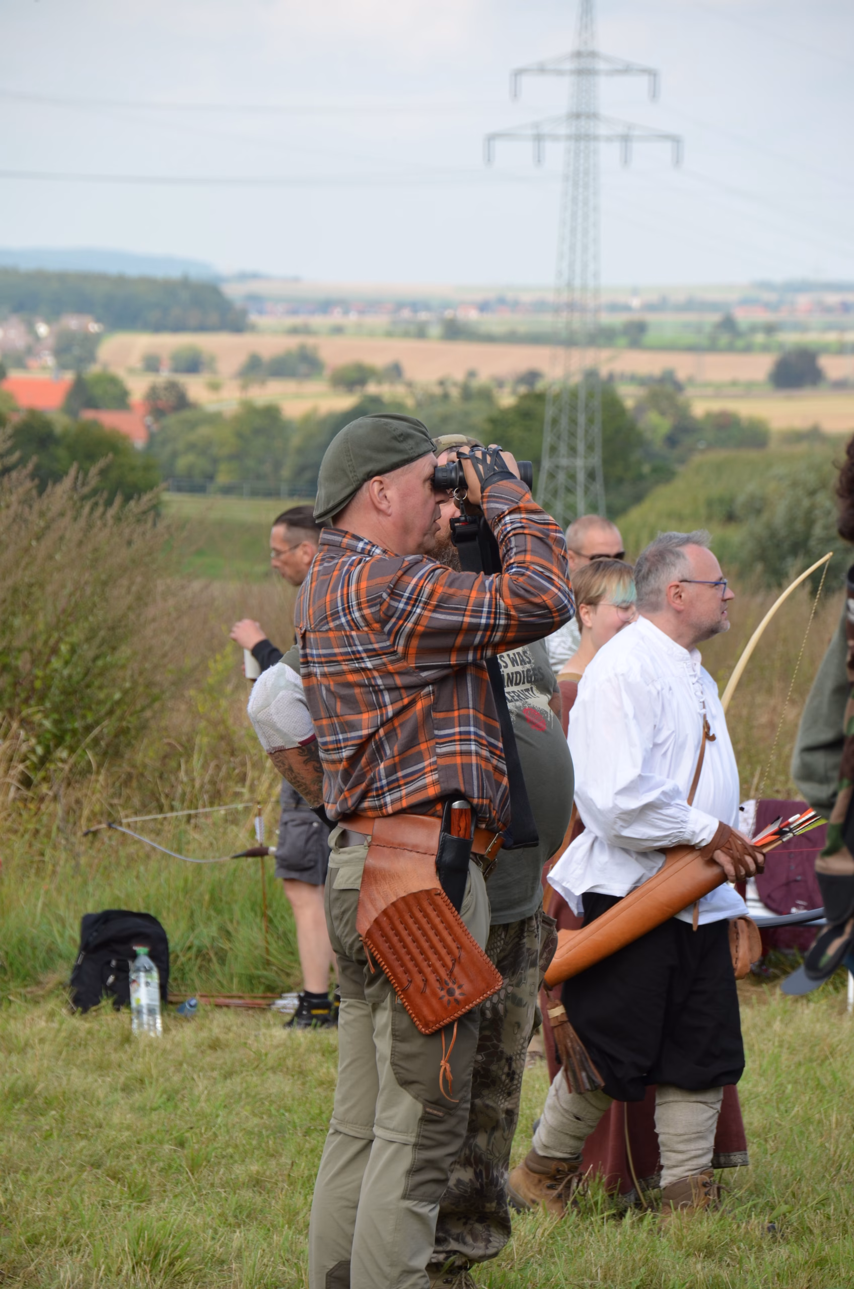 Bogenschütze mit Fernglas beobachtet das Ziel beim Clout-Bogenschießen in Siebenberge 2021, veranstaltet von Pfeilflugkunst.