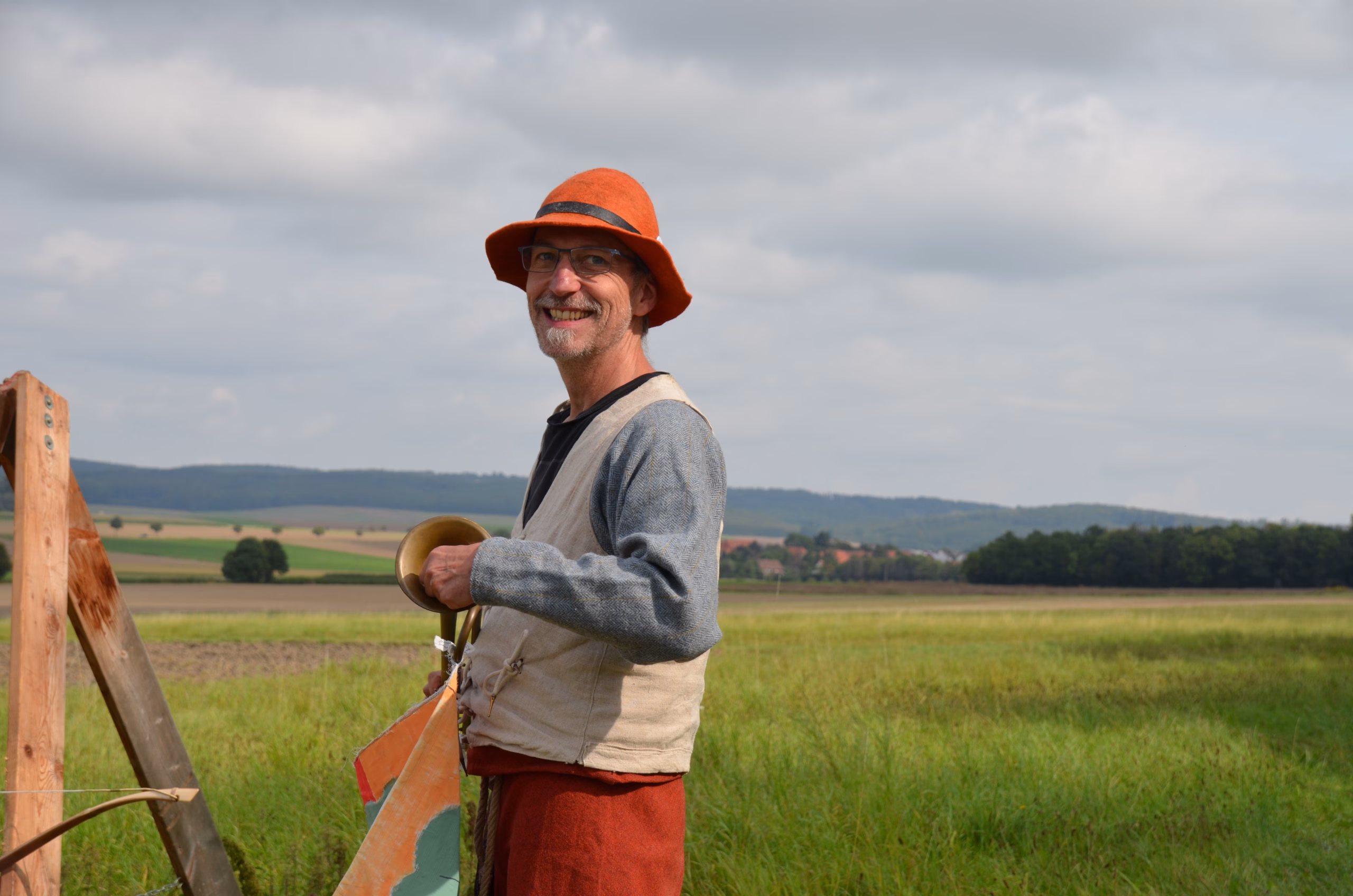 Lächelnder Mann mit orangefarbenem Hut und Glocke beim Siebenberge Clout Bogenwettbewerb 2021 von Pfeilflugkunst