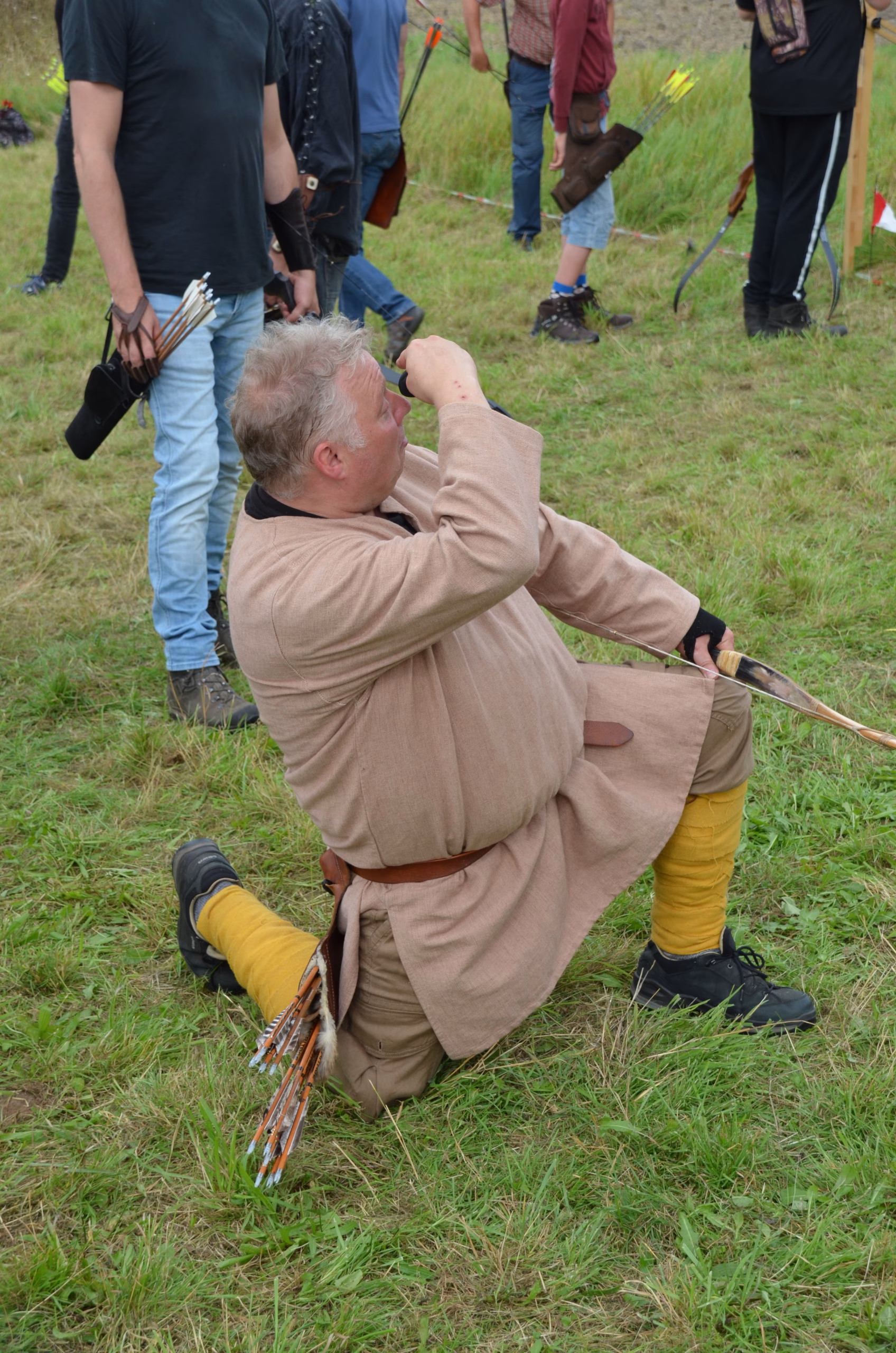 Ein Bogenschütze in traditioneller Kleidung kniet beim Siebenberge Clout Bogenwettbewerb 2021 und beobachtet das Ziel durch ein Monokular. Veranstalter: Pfeilflugkunst.