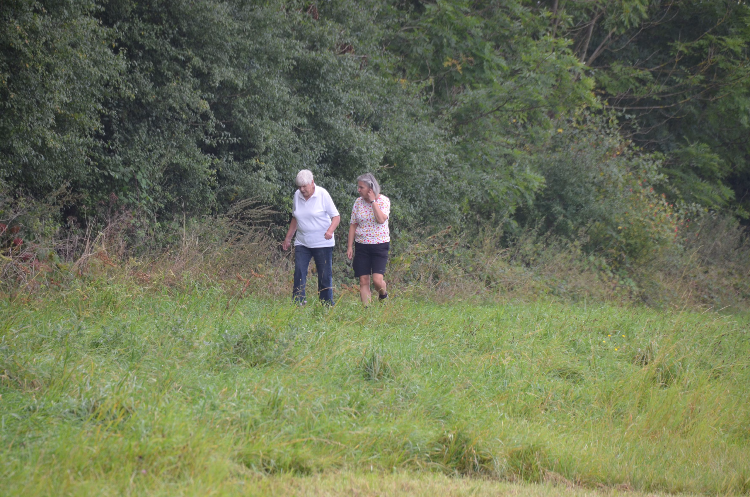 Zwei Frauen gehen durch ein grünes Feld beim Siebenberge Clout Bogenwettbewerb von Pfeilflugkunst.
