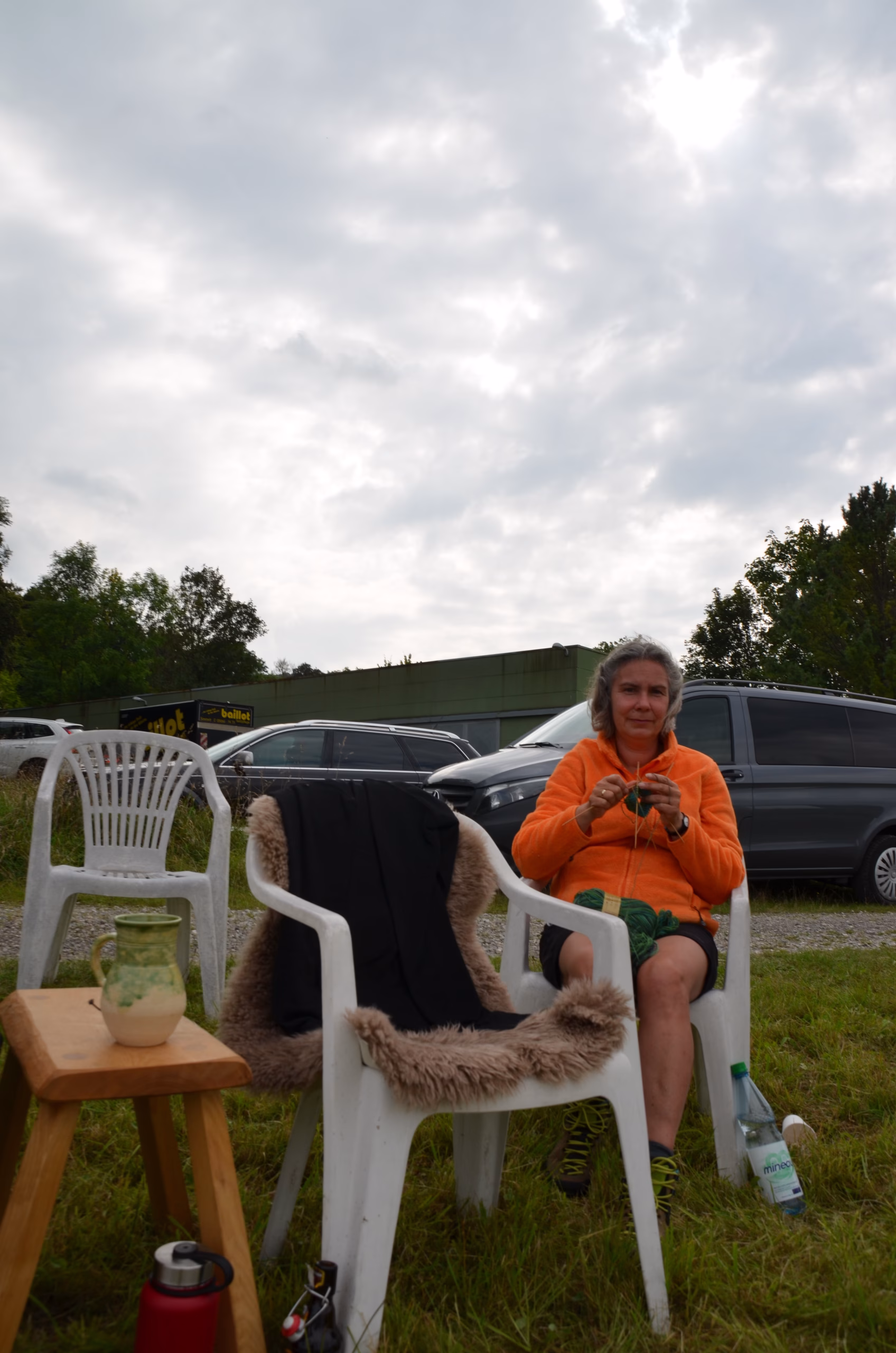 Eine Frau in orangefarbener Jacke strickt auf einem Stuhl sitzend während einer Pause beim Siebenberge Clout Bogenwettbewerb 2021.