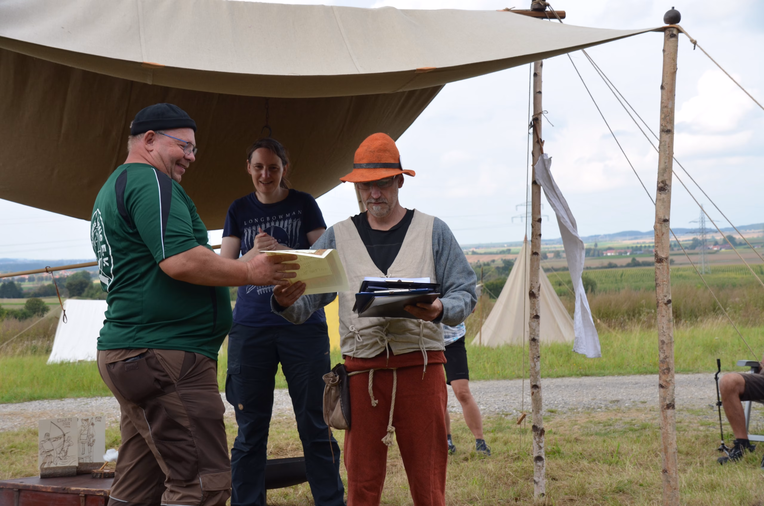 Teilnehmer und Organisatoren von Pfeilflugkunst bei der Auswertung des Siebenberge Clout Bogenwettbewerbs 2021 unter einem Zelt im Freien.