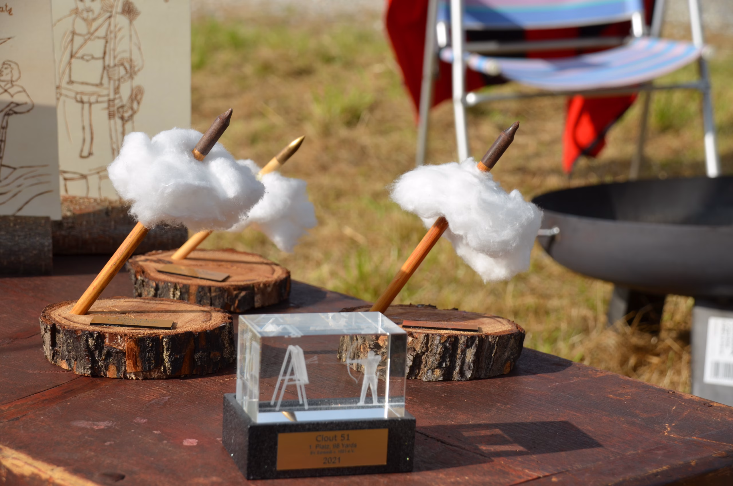Trophäen und Pokale des Siebenberge Clout Bogenwettbewerbs 2021 von Pfeilflugkunst, darunter kreative Pfeil-Wolken-Skulpturen und ein Acryl-Pokal.