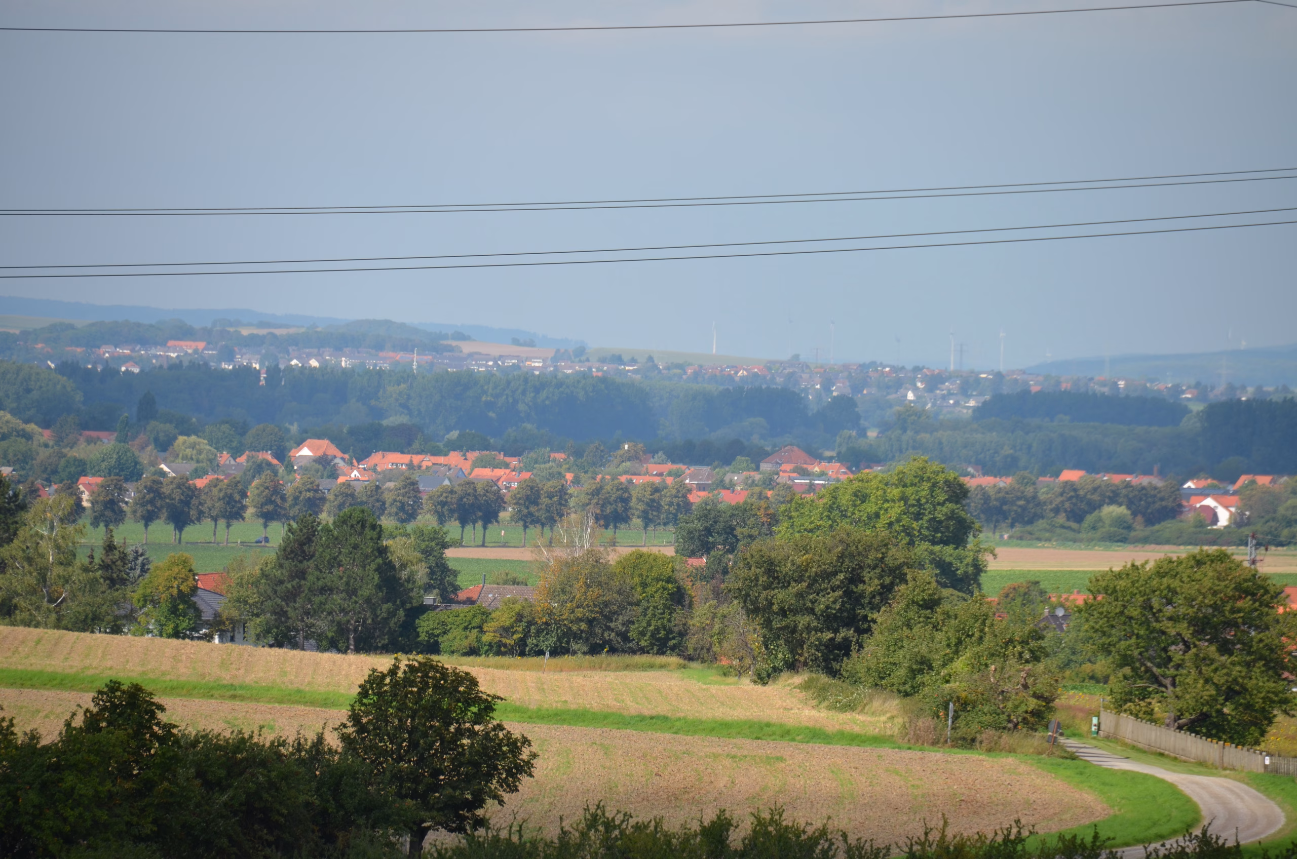 Malerische Landschaft der Siebenberge mit Feldern, einem Dorf mit roten Dächern und Windrädern am Horizont, aufgenommen beim Clout-Bogenwettbewerb von Pfeilflugkunst.