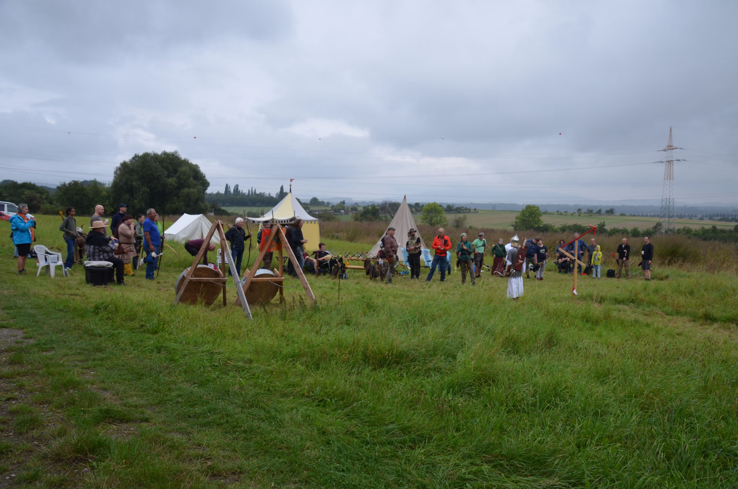 Gruppenbild von Bogenschützen und Zuschauern beim Siebenberge Clout Bogenwettbewerb 2021, veranstaltet von Pfeilflugkunst, auf einem grünen Feld mit Zelten.
